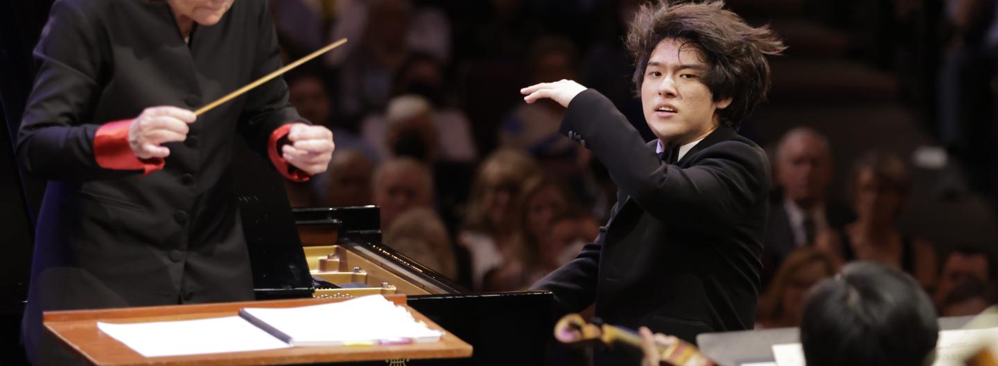 Yunchan Lim playing the piano with his hair flying up and facing the orchestra