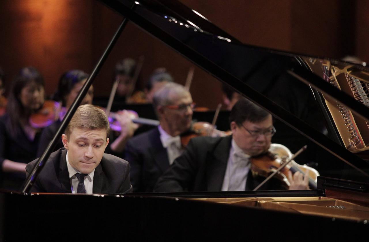 Close up of Dmytro Choni playing the piano with the orchestra behind him